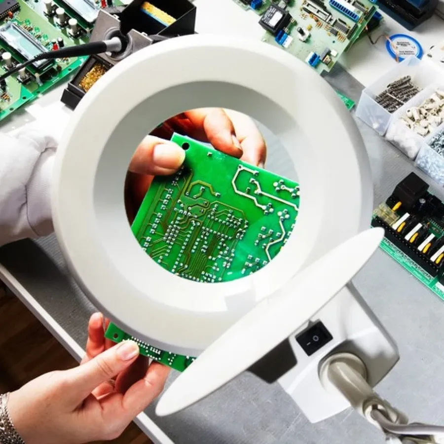 A person inspecting a PCB using a magnifying tool.